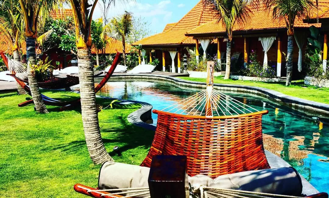 Woven hammock near a swimming pool and tropical bungalows